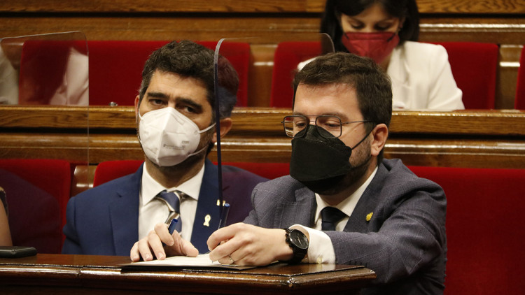 Pla mitjà del president de la Generalitat, Pere Aragonès, escrivint en un paper, i al costat el vicepresident Jordi Puigneró als escons de l'hemicicle del Parlament el 2 de juny del 2021. Agència Catalana de Notícies