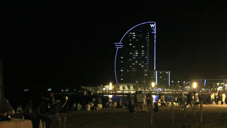 Grups de persones socialitzant de nit a la platja de Sant Miquel de Barcelona, amb el conegut com a Hotel Vela al fons. 10 de juliol del 2021. Agència Catalana de Notícies