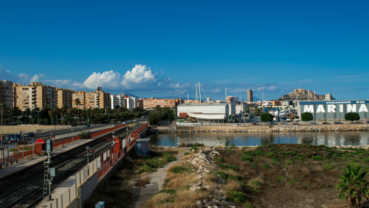 Panoràmica de la part marítima del barri de Sant Gabriel, amb la desembocadura del barranc de les Ovelles, les vies ferroviàries que travessen el barri, la zona estibadora del port, els habitatges a tocar i el castell alacantí de Santa Bàrbara de fons.. David Correoso