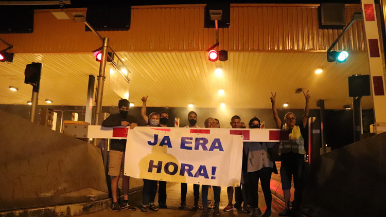 Pla contrapicat dels veïns de Sant Julià de Ramis aguantant una pancarta per celebrar la finalització de la concessió de l'AP-7 amb el peatge de Girona Nord al darrera la mitjanit del 31 d'agost de 2021. Agència Catalana de Notícies