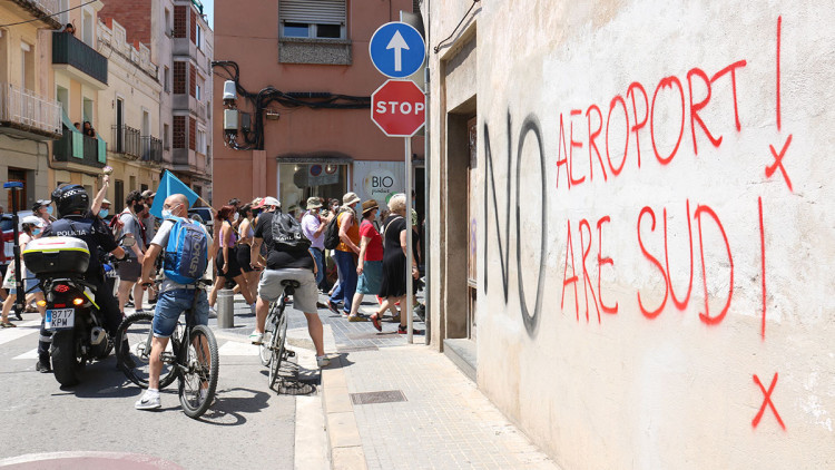 Pla general de la manifestació contra l'ARE Sud i l'ampliació de l'aeroport al Prat de Llobregat i una pintada en contra dels projectes, el 12 de juny de 2021. Agència Catalana de Notícies