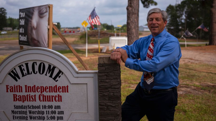 Cartell de benvinguda a la parròquia Faith Independent Baptist Church. Al costat de la placa d'entrada, el pastor evangèlic Doug Lovett, amb una corbata de la bandera nord-americana