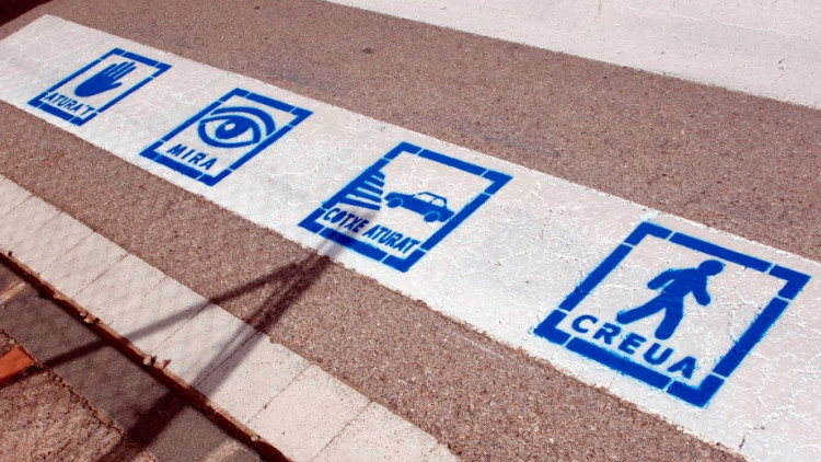Quatre pictogrames en color blau pintats en alguns passos de vianants de Roquetes (Baix Ebre) per millorar l'autonomia i la seguretat de les persones amb autisme. Agència Catalana de Notícies